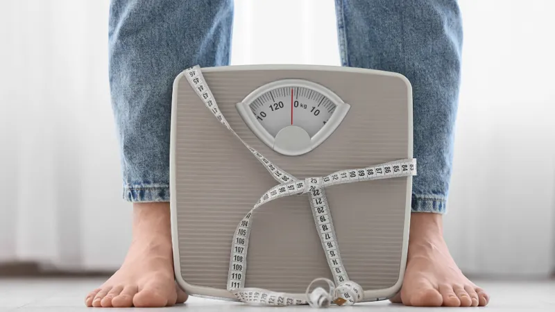 Legs Of Woman In Jeans And Weight Scales With Tape Measure At Home, Closeup