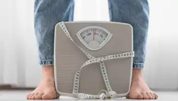 Legs Of Woman In Jeans And Weight Scales With Tape Measure At Home, Closeup