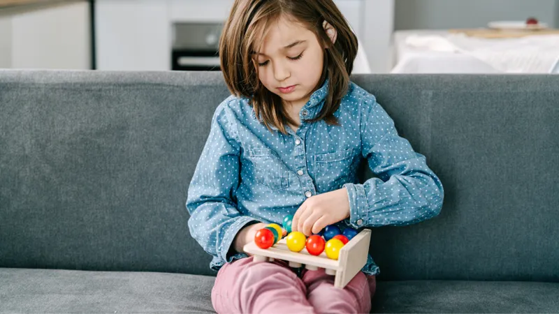 A Girl Sitting On Couch While Playing A Toy
