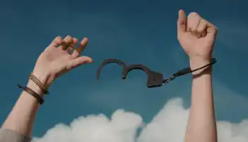 Hands Breaking Free From Handcuffs Against A Blue Sky